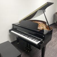 Black Yamaha grand piano in showroom, open lid, with bench.