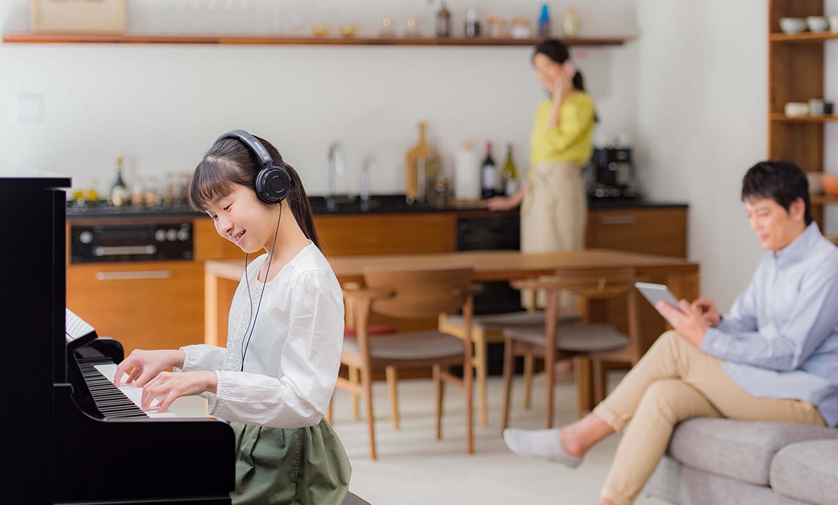Young girl playing a digital piano with headphones, enjoying music in a modern home setting. Perfect for family entertainment.