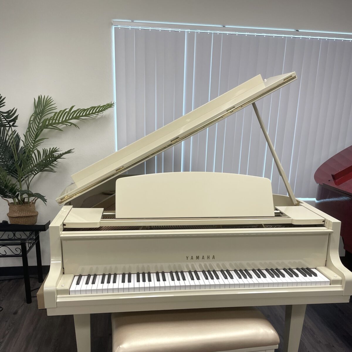 Alt text: Yamaha baby grand piano in polished ivory finish, featuring a matching padded bench, perfect for any music enthusiast.