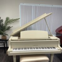 Alt text: Yamaha baby grand piano in polished ivory finish, featuring a matching padded bench, perfect for any music enthusiast.